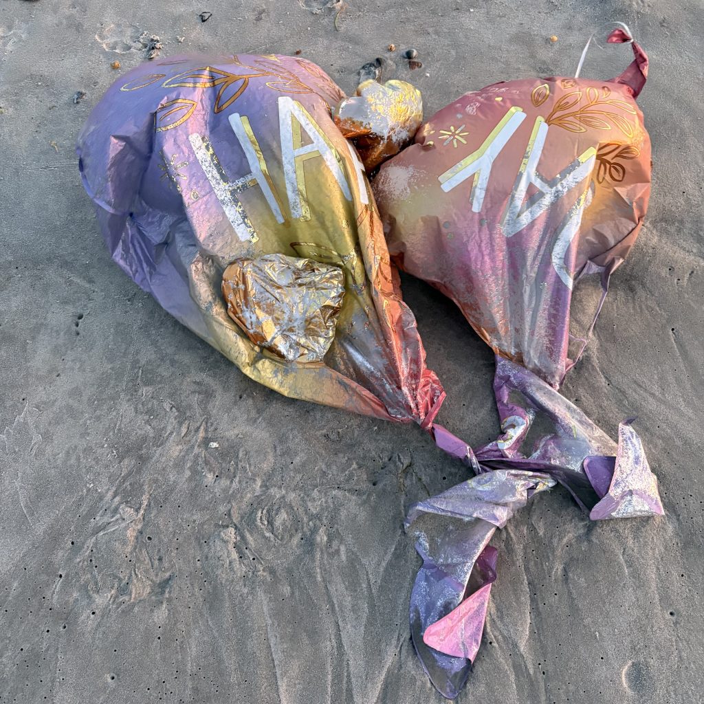Two pastel gradient mylar balloons tangled on the beach, partially buried in sand