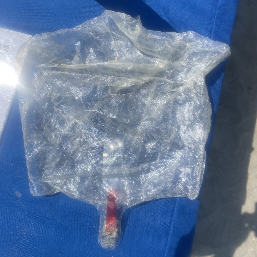 A mylar balloon that is so degraded it is now clear and crinkled sits on a blue tablecloth outdoors.